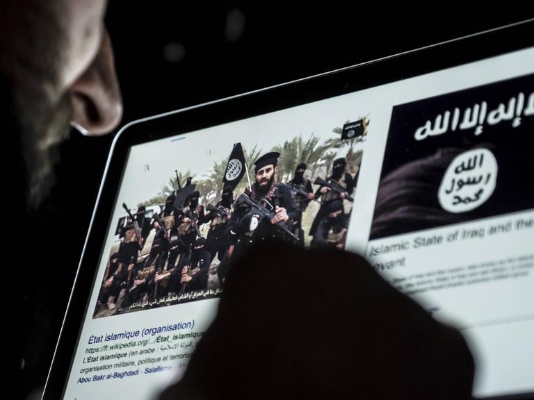 Ein Mann blickt auf einen Computerbildschirm mit der Flagge des sogenannten Islamischen Staates und einem Bild mit Kämpfern, die die Flagge des Islamischen Staates tragen.