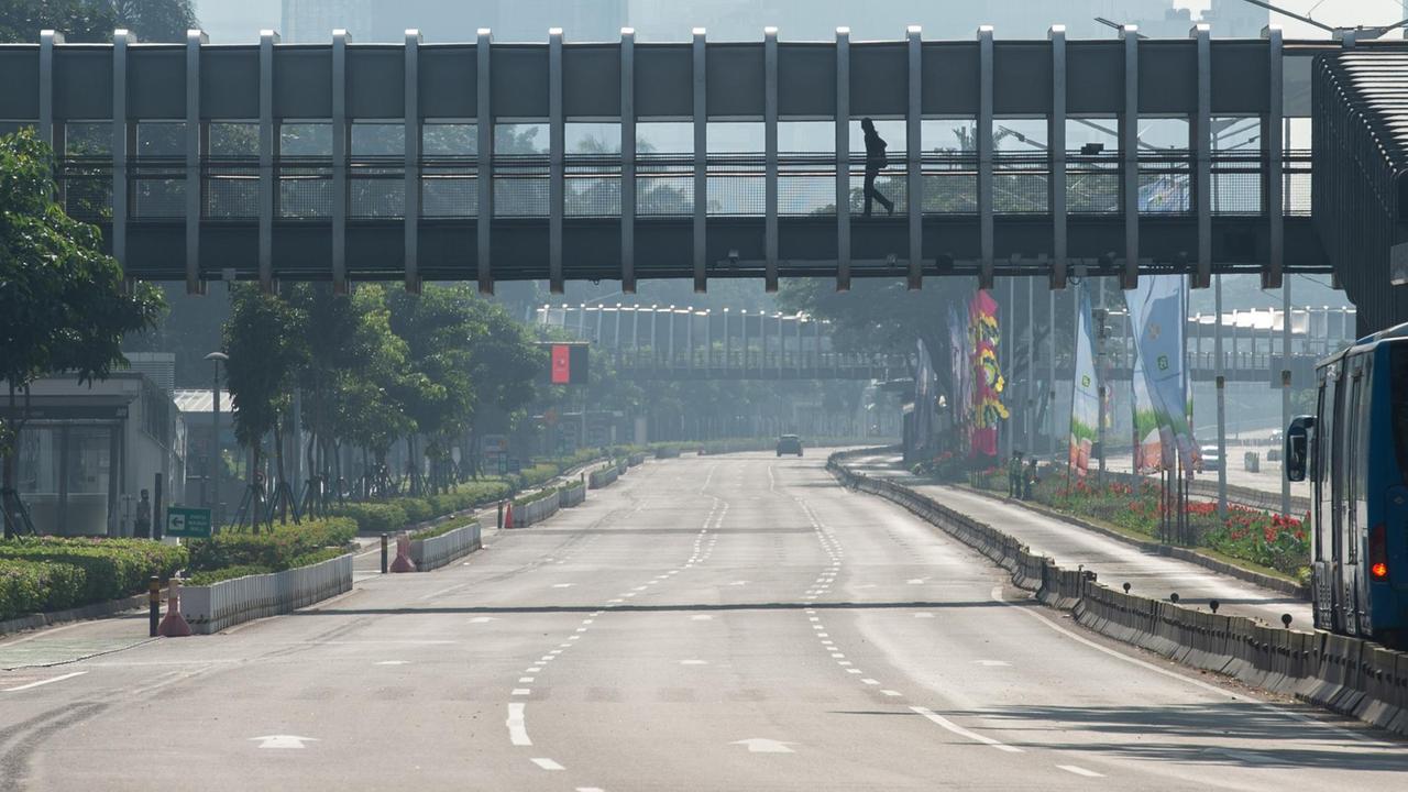 Eine Person geht in Jakarta über eine Fußgängerbrücke, die über eine gesperrte und unbefahrene Straße führt. 