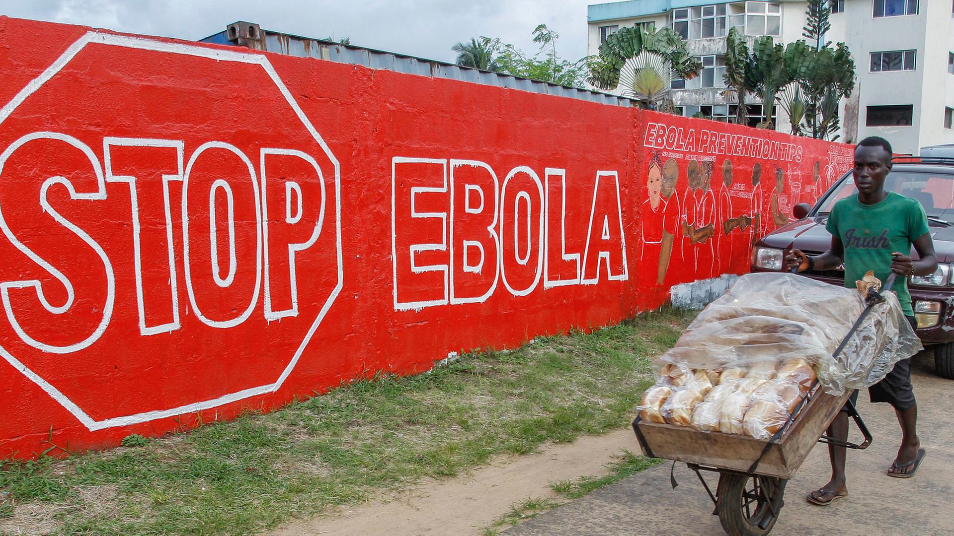 Ein Mann schiebt am 15. September 2014 in der liberianischen Hauptstadt Monrovia eine Karre mit Brot über eine Straße. Im Hintergrund hängt ein Schild mit der Aufschrift Stop Ebola.