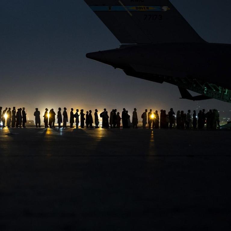 Eine Menschenschlange, die in das geöffnete Heck eines Flugzeugs führt, bei Nacht. 