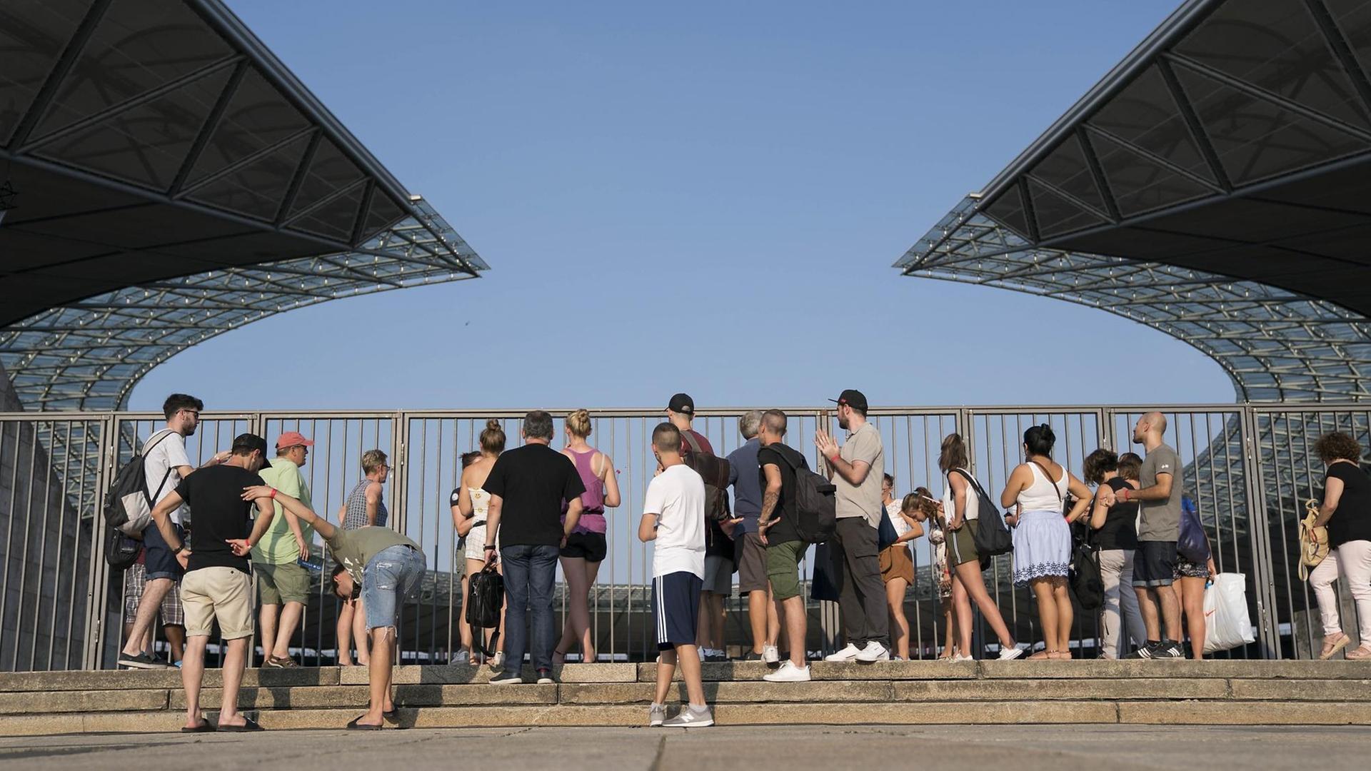 Besucher stehen vor der Umzäunung des Berliner Olympiastadions und blicken hinein.