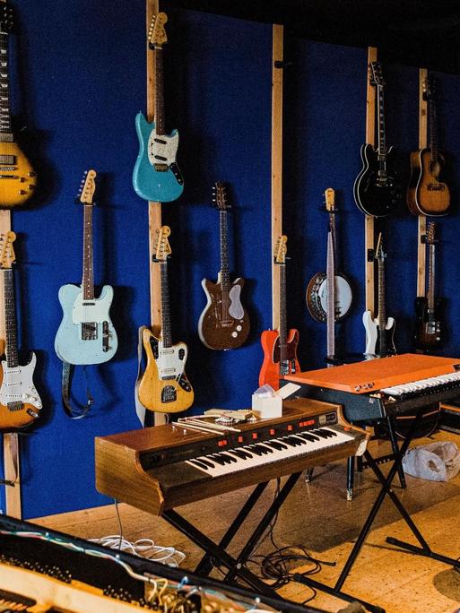 In einem Tonstudio in Reykjavík hängen Gitarren an der Wand, ein offener Flügel steht im Vordergrund, mehrere weitere Tasteninstrumente sind zu sehen, in der Mitte steht ein Hocker.