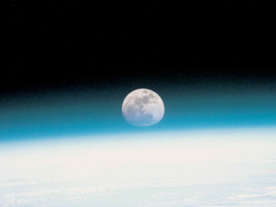Eine Aufnahme aus der obersten Atmosphärenschicht. Der Himmel ist schwarz, unten die Erde blau, hinter dem Horizont geht der Mond auf.