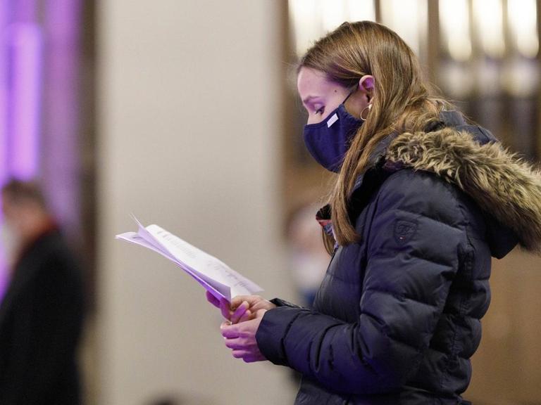 Eine junge Kirchengängerin singt während des Gottesdienstes. Sie trägt einen Mundschutz.