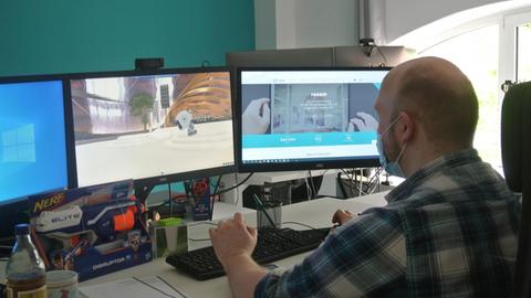 Hendrik Lober am Schreibtisch mit drei Monitoren. Er arbeitet an Nuland mit Avatar.