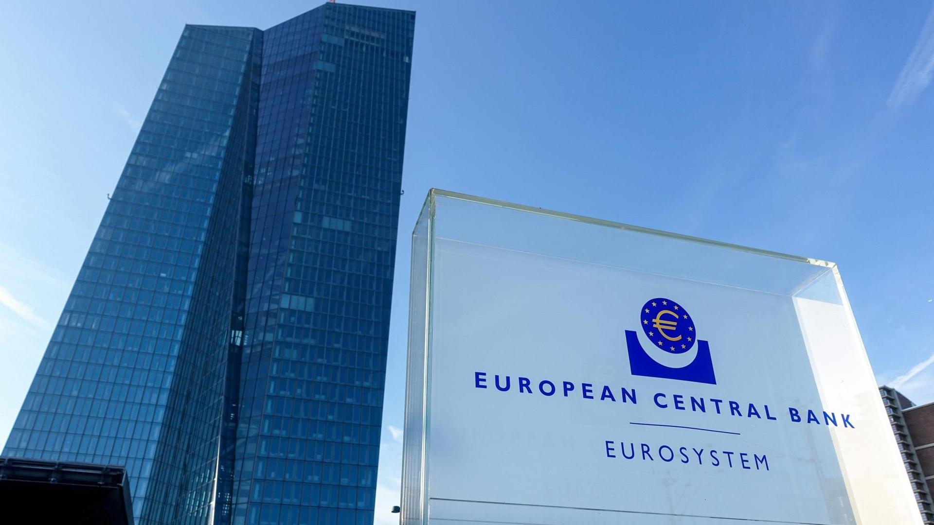 Totale des Gebäudes der Europäischen Zentralbank von unten, im Vordergrund ein Schild, worauf "European Central Bank / Eurosystem" zu lesen steht