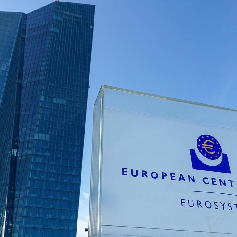 Totale des Gebäudes der Europäischen Zentralbank von unten, im Vordergrund ein Schild, worauf "European Central Bank / Eurosystem" zu lesen steht