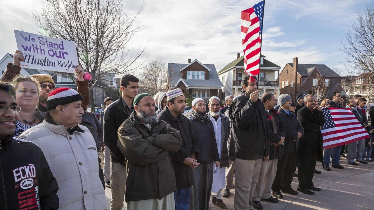 Muslime und Nicht-Muslime stehen mit Schildern und US-Flaggen nebeneinander auf der Straße