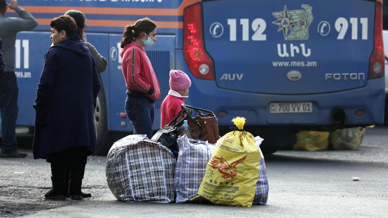 Eine Frau mit Kind steht mit gepackten Taschen vor einem Bus.