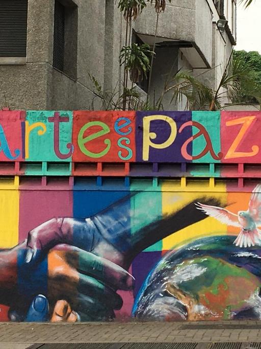 Streetart in Venezuala: Ein Graffito mit der Aufschrift "arte es paz", einer angeschnittenen Weltkugel, einer weißen Taube und zwei einander greifenden Händen