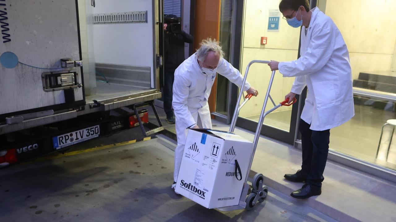 Mitarbeiter transportieren einen Karton mit einigen der ersten knapp 10.000 Dosen Corona-Impfstoff für Thüringen in ein Gebäude.
