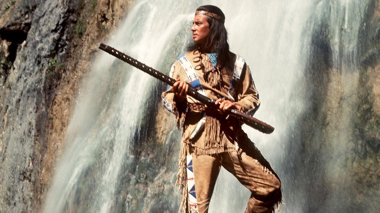 Pierre Brice als Häuptling "Winnetou" vor Kulisse eines Wasserfalls.