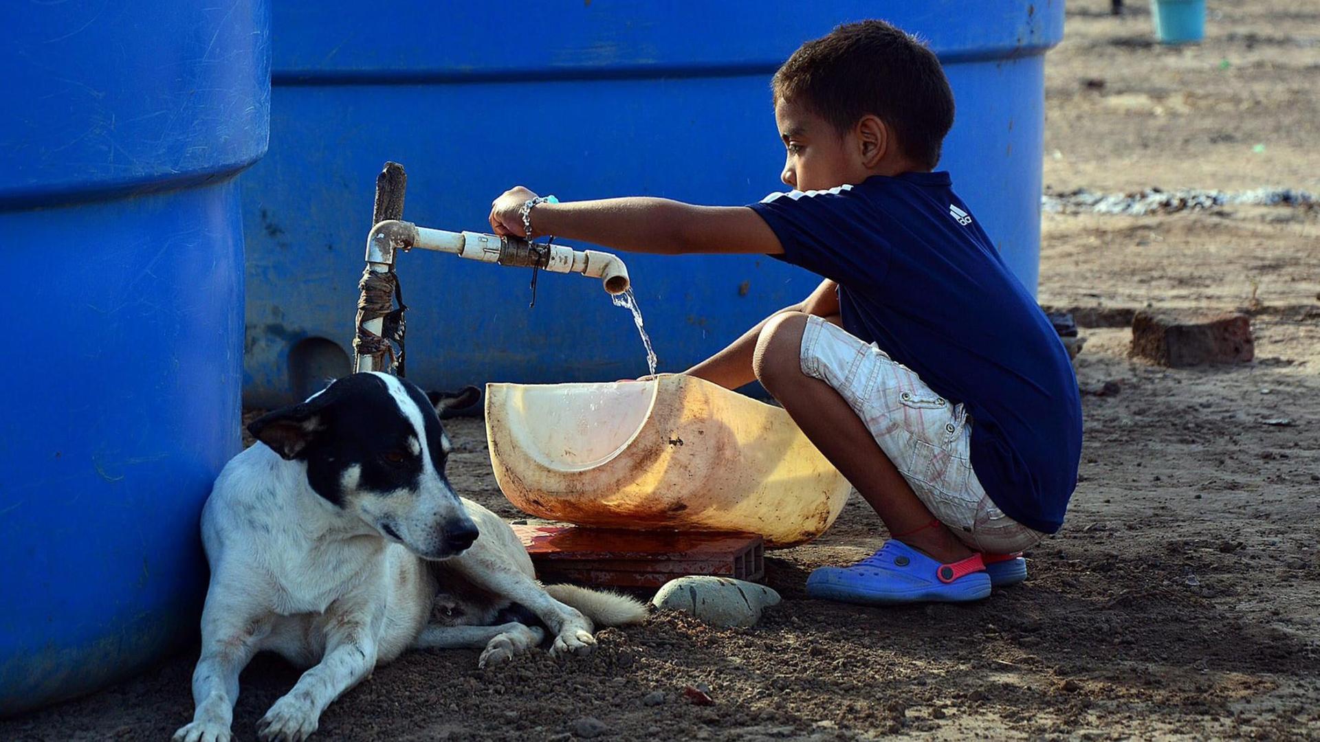 Ein Junge in Kolumbien füllt Wasser aus einem Tank in ein Plastikgefäß.