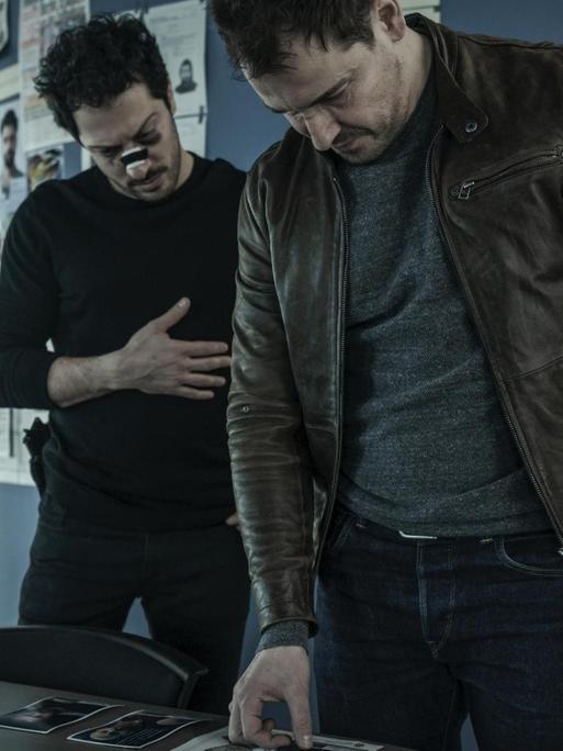 Zwei Schauspieler der Netflix-Serie "Dogs of Berlin" stehen an einem Schreibtisch