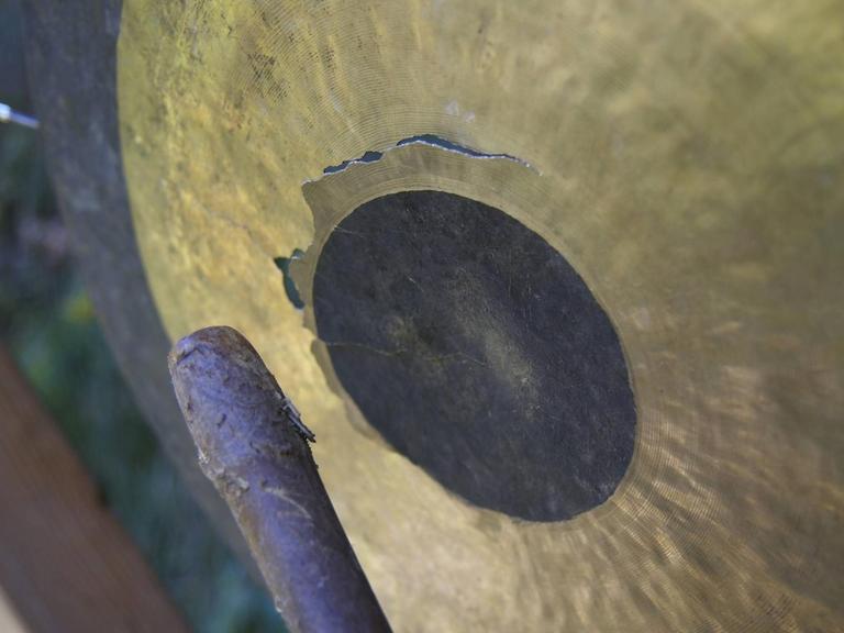 Ein goldfarbener Gong wird mit einem Schlegel aus Holz geschlagen.