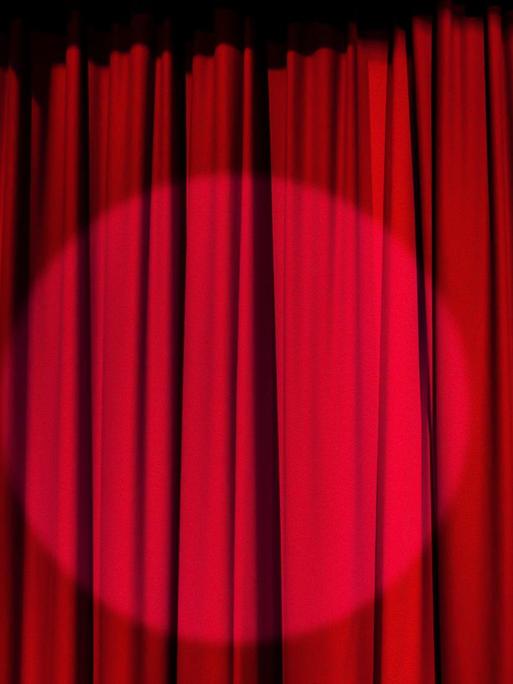 Auf dem Foto sieht man einen Scheinwerfer, auf einen roten Theater-Vorhang gerichtet.