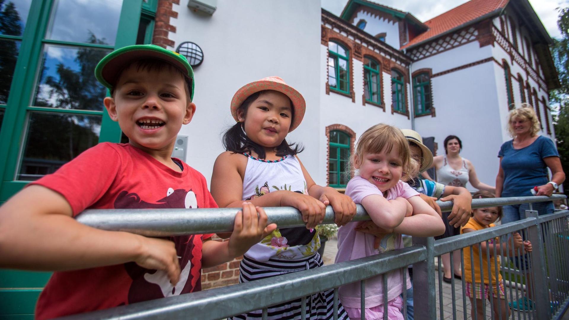 Kinder stehen lachend auf dem Balkon von einem Kindergarten