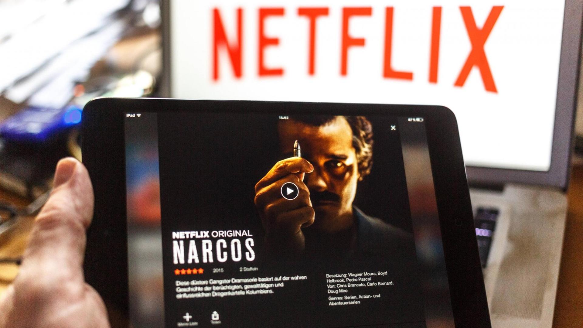Ein iPad mit "Narcos" wird ins Bild gehalten, im Hintergrund ist der Schriftzug Netflix zu sehen.