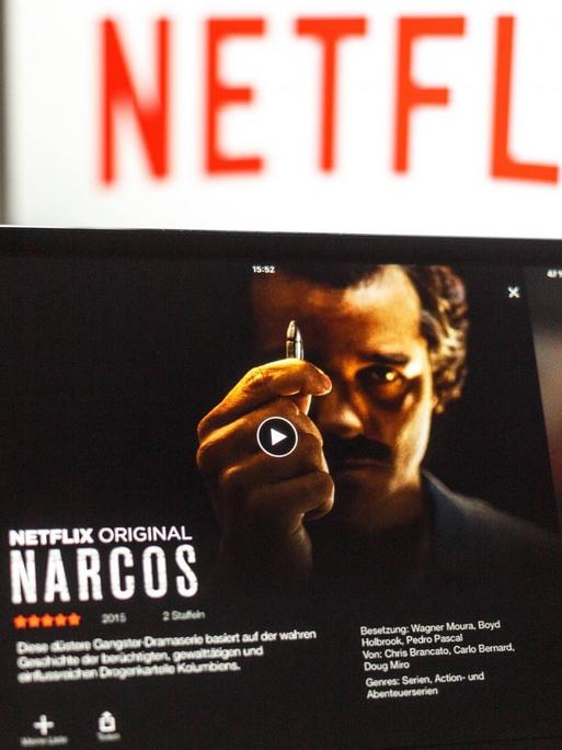 Ein iPad mit "Narcos" wird ins Bild gehalten, im Hintergrund ist der Schriftzug Netflix zu sehen.