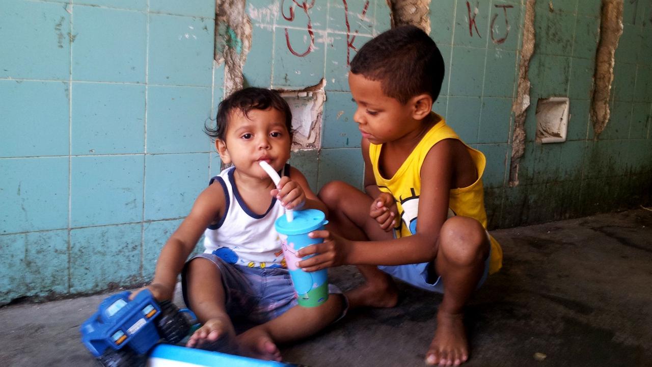 Ein Junge reicht einem anderen Kind eine Trinkflasche.
