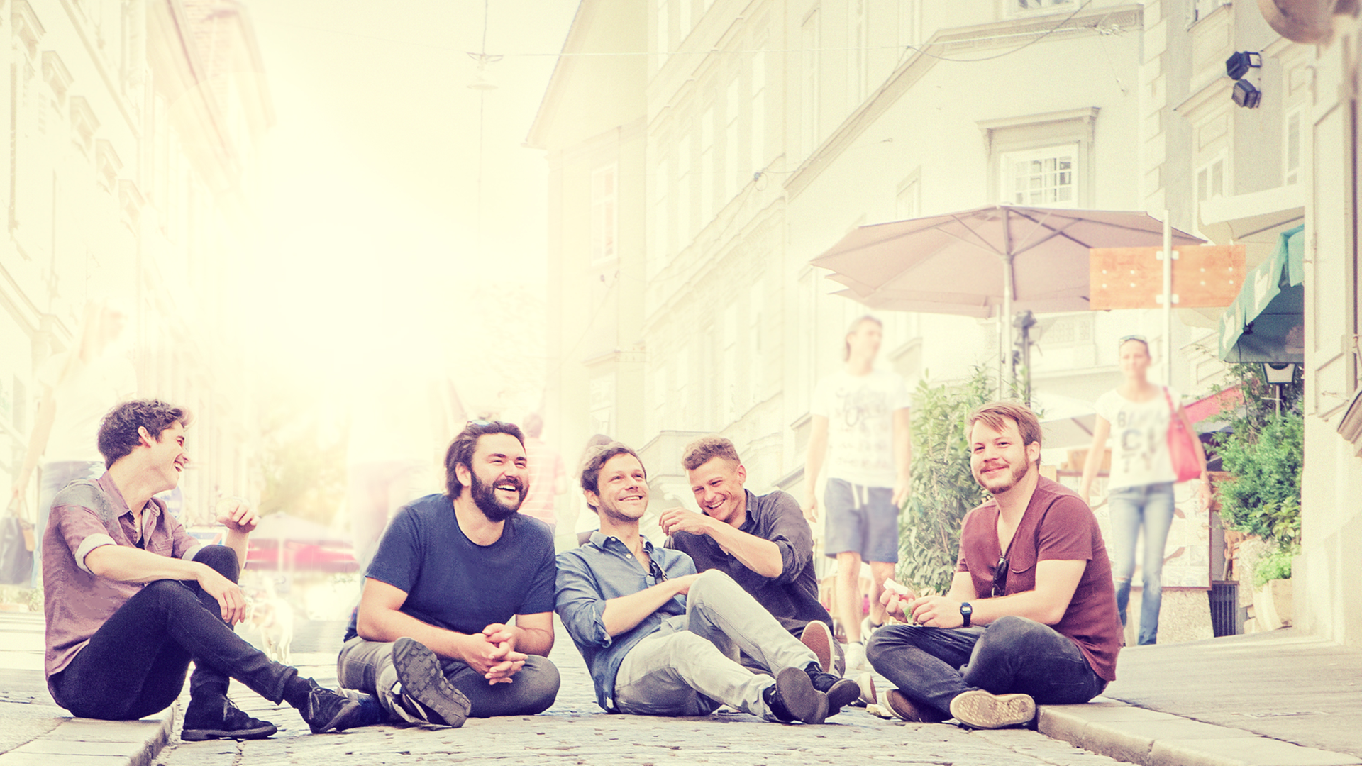 Die Band Granada: Die fünf Musiker sitzen lachend auf einer Straße.