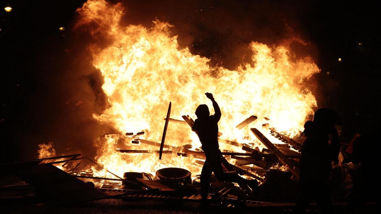 Sie sehen einen Demonstranten vor einem großen Feuer in Paris.