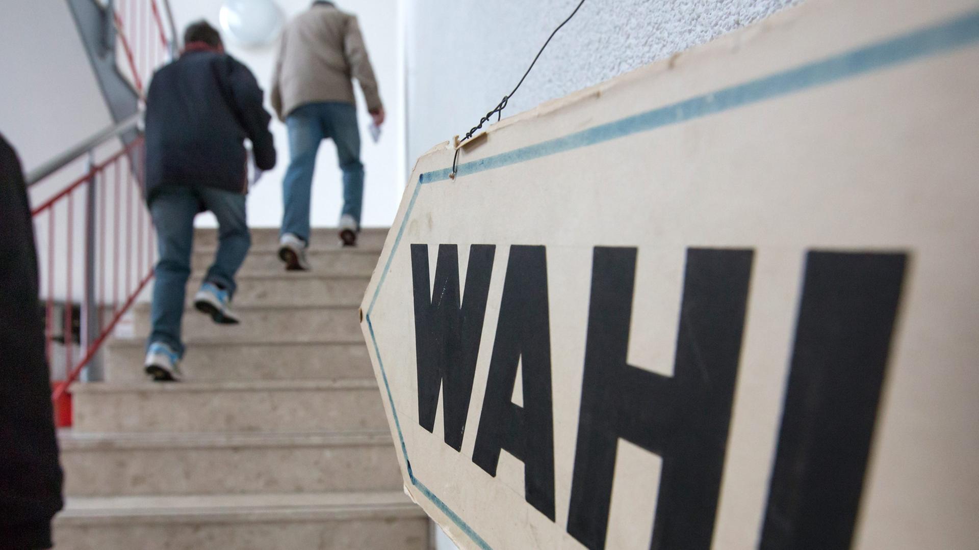 Ein Schild mit dem Wort "Wahl" hängt weist den Weg eine Treppe hinauf, Menschen gehen die Treppe hinauf