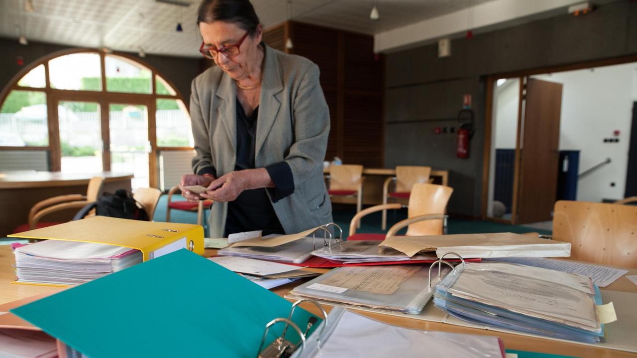 Denise Vallat steht vor einem Tisch voller Akten.