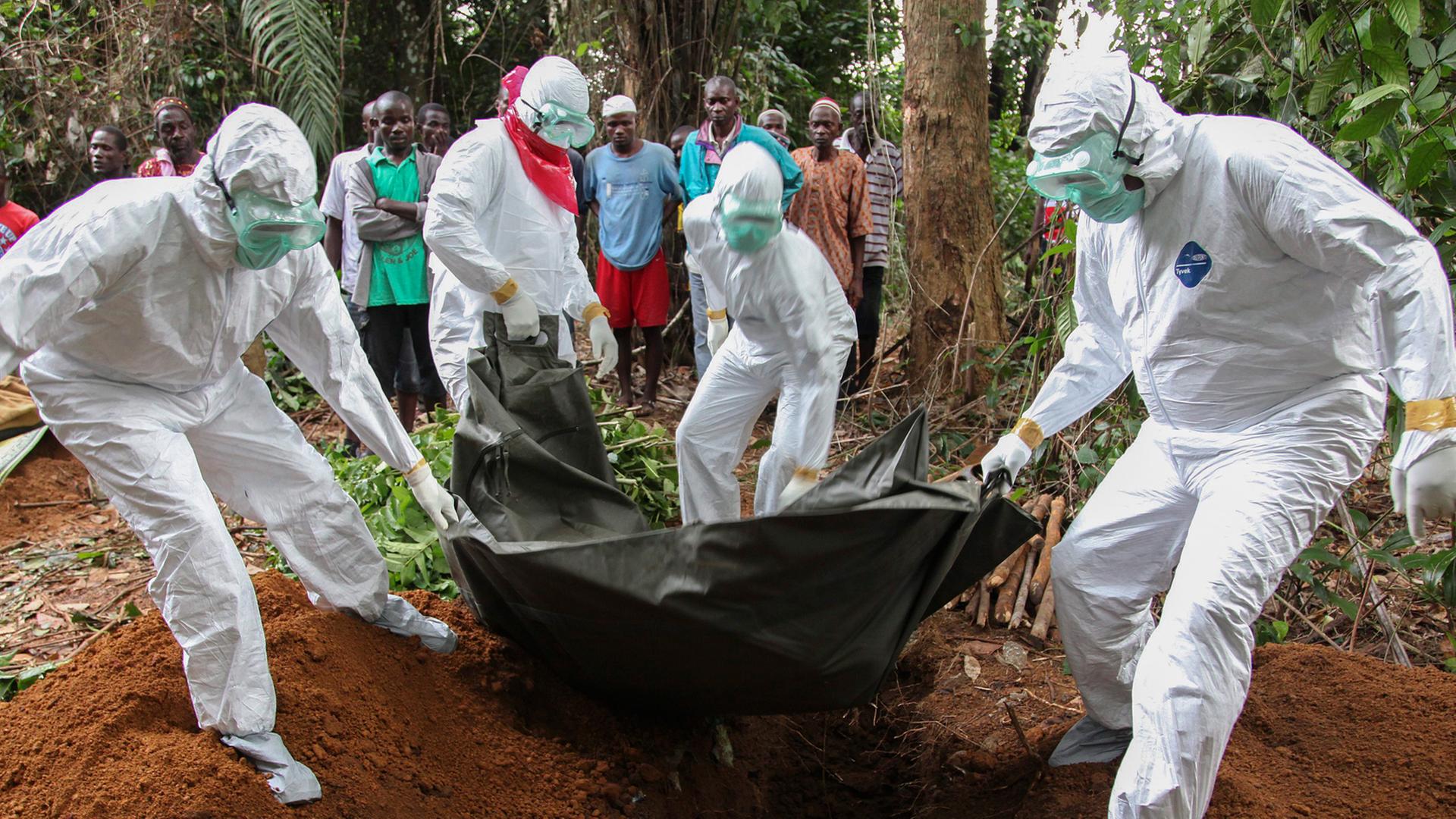 Ein Ebola-Toter wird von Menschen in Schutzanzügen beerdigt.