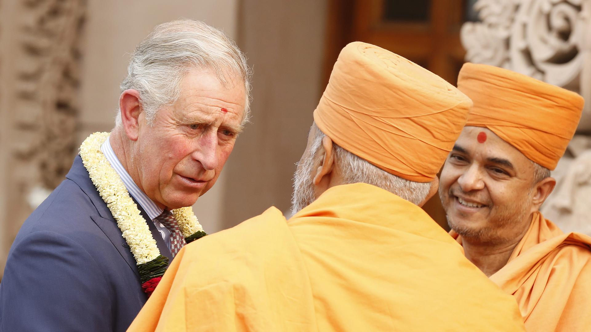Prince Charles im Gespräch mit zwei in orange gekleideten Mönchen in Neu-Delhi, Indien