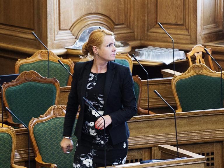 Inger Stojberg, Dänemarks Ministerin für Integration, rote Haare, schwarz-weißes Kostüm, geht zwischen Stühlen im Parlament entlang.
