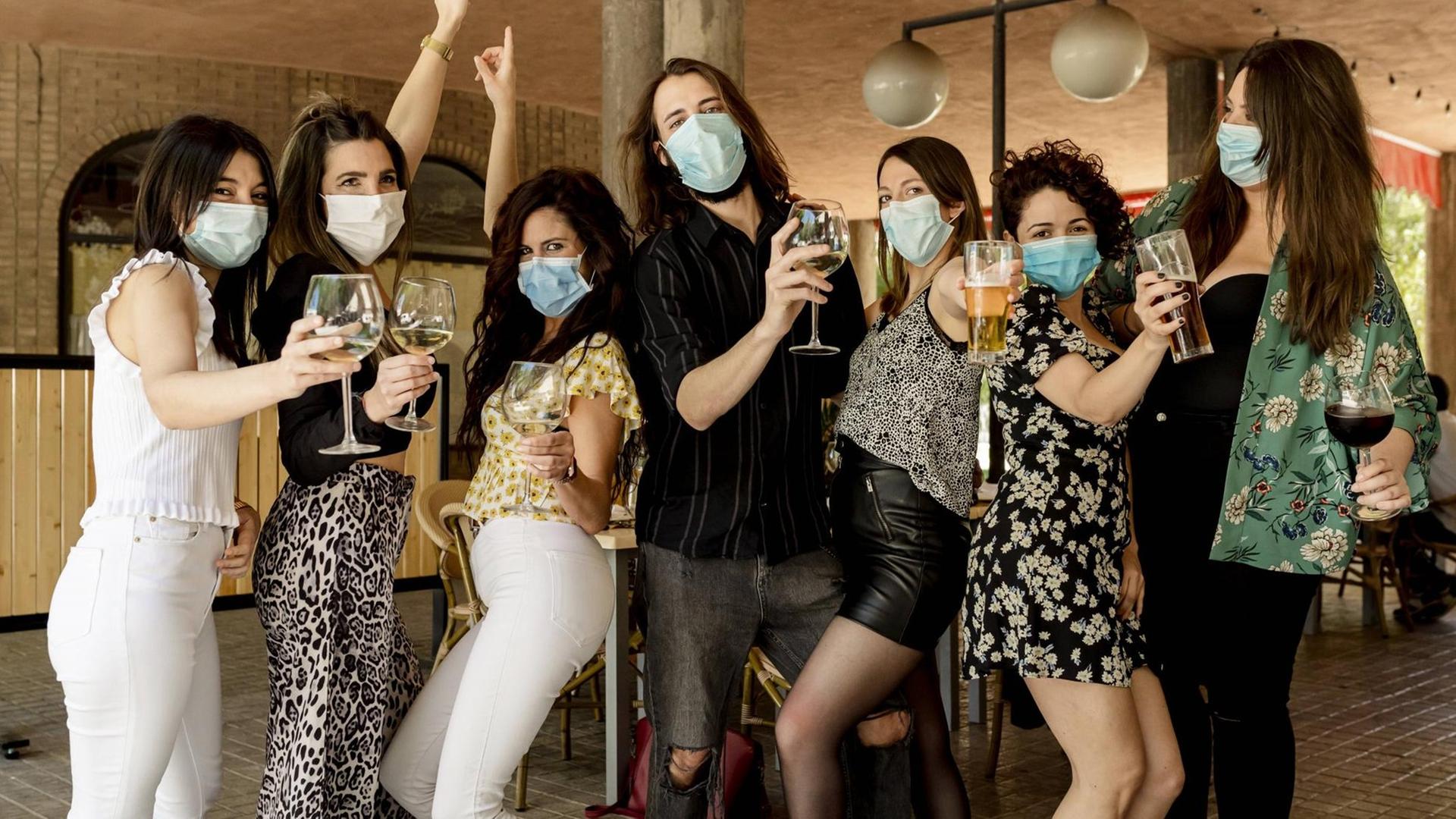 Junge Leute feiern bei einer Party und tragen einen Mund-Nasen-Schutz gegen eine mögliche Infektion.