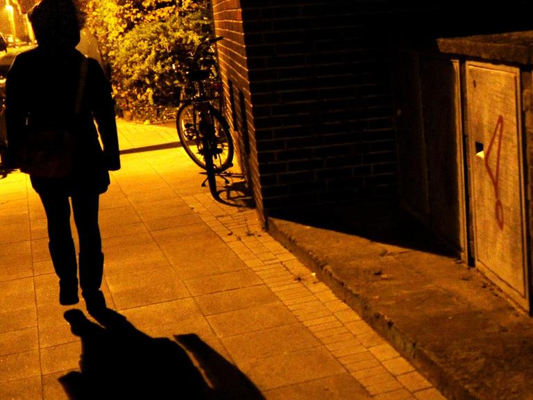 Eine Frau geht im Licht der Straßenlaternen alleine über eine dunkle Straße