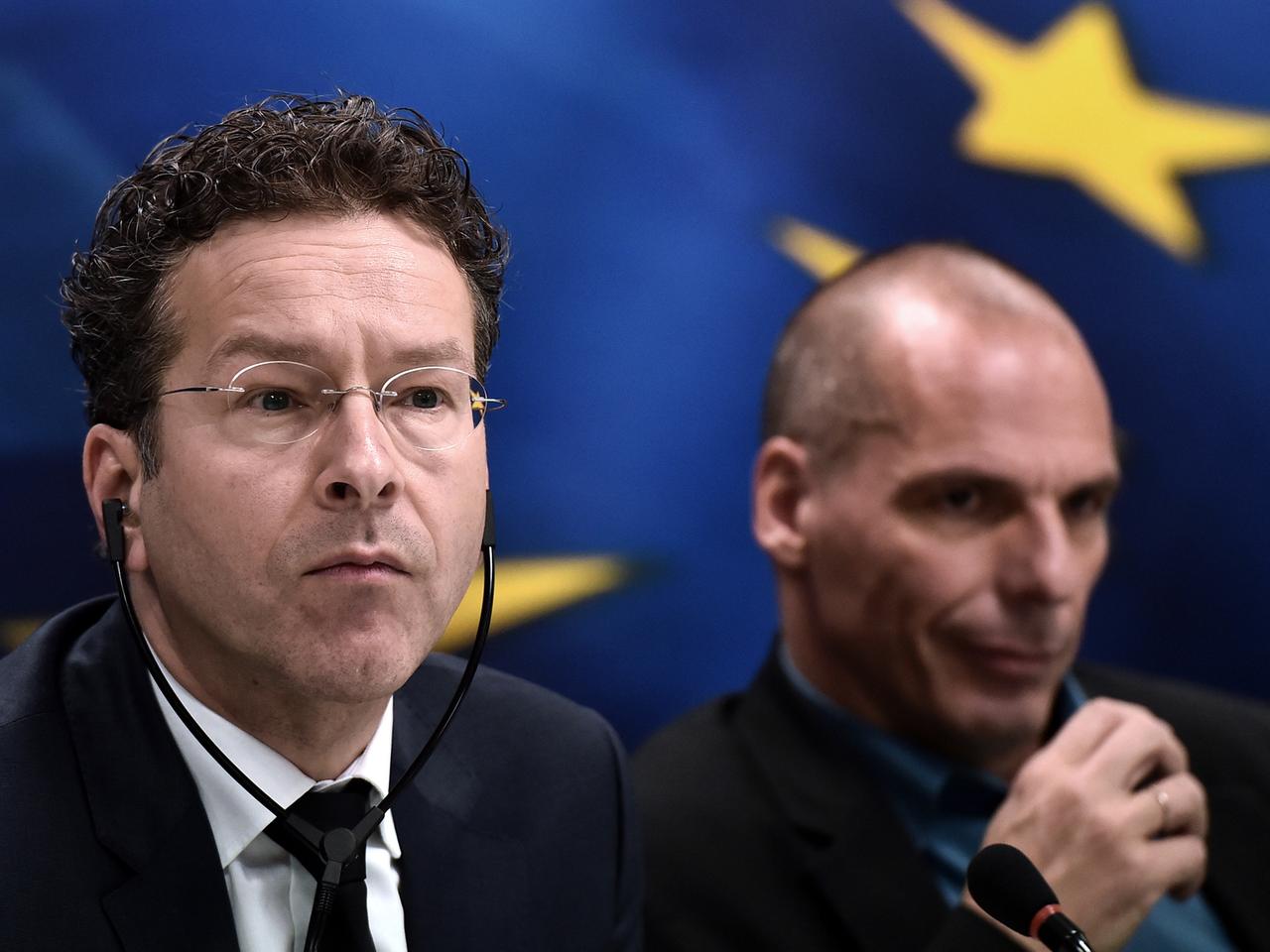 Eurogruppenchef Jeroen Dijsselbloem und der griechische Finanzminister Yanis Varoufakis bei einer Pressekonferenz in Athen. Dijsselbloen trägt einen Kopfhörer. Im Hintergrund ist die Europa-Fahne.