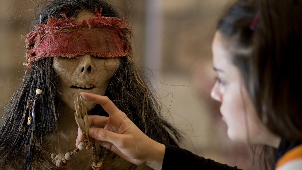 Filmausschnitt aus dem Film "La Flor". Eine zombiehafte Gestalt mit roter Augenbinde wird von einem Mädchen gefüttert