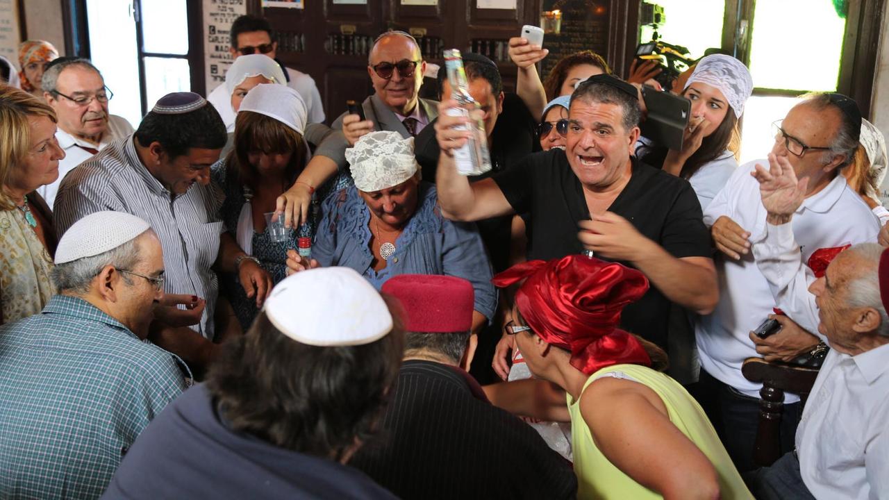 Eine Gruppe von Menschen in der Synagoge La Ghriba auf der tunesischen Insel Djerba. Ein Mann hält eine Flasche mit Feigenschnaps, auf Djerba "Boukha" genannt, in die Höhe. Der Schnaps ist Teil eines Rituals, das zum jüdischen Fest Lag baOmer gehört. Foto: imago stock&people