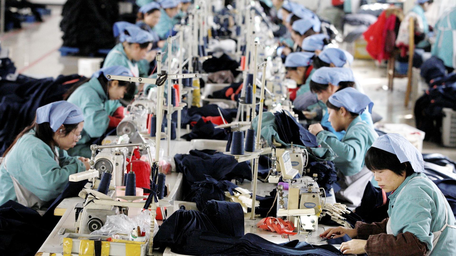 Etwa 20 Arbeiterinnen konzentrieren sich an einem langen Tisch auf ihre Nähmaschinen.