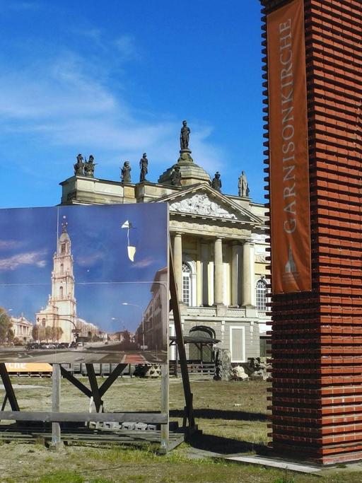 Blick auf die Freifläche der ehemaligen Garnisonkirche an der Breiten Strasse in Potsdam. Eine ausgestellte Fotografie der Kirche und ein Torbogen im Vordergrund erinnern.