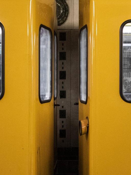 Zwei Personen mit Mund-Nasen-Maske sitzen in unterschiedlichen Waggons der Berliner U-Bahn.