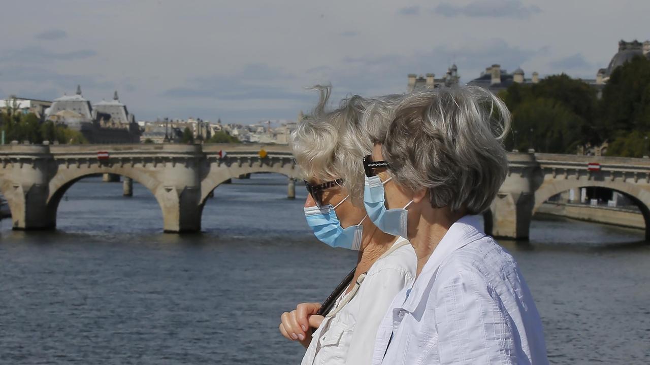 Zwei Passantinnen mit medizinischem Mundschutz spazieren über eine Brücke über die Seine.
