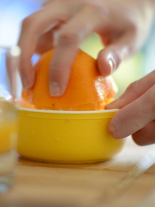 Eine Frau presst eine Orange aus, im Vordergrund ein Glas mit Orangensaft.