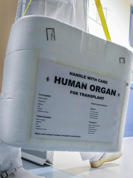 Pfleger trägt eine Box mit der Aufschrift "Human Organ" durch einen Krankenhausflur