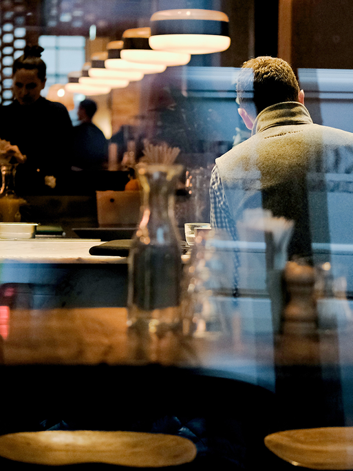 Ein Mann steht in einer Bar an einem Tresen. Man sieht ihn von draußen durch das Schaufenster.