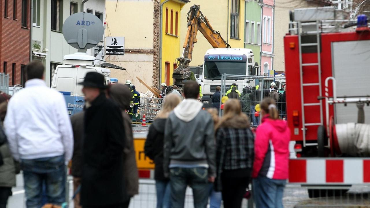 Schaulustige gucken hinter einer Absperrung zum explodierten Wohnhaus in Brühl.
