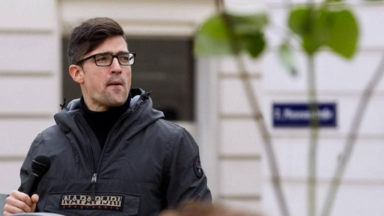 Martin Sellner in einer schwarzen Jacke steht an einem Rednerpult und schaut nach links. Dahinter unscharf eine weiße Hauswand. Martin Sellner in einer schwarzen Jacke steht an einem Rednerpult und schaut nach links. Dahinter unscharf eine weiße Hauswand.
