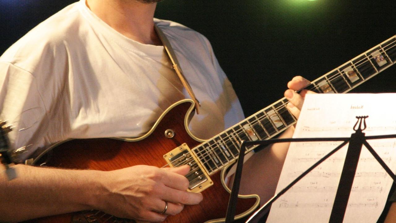 Ein Gitarrist steht vor einem Notenständer und spielt. Der Kopf ist außerhalb des Bildausschnittes.