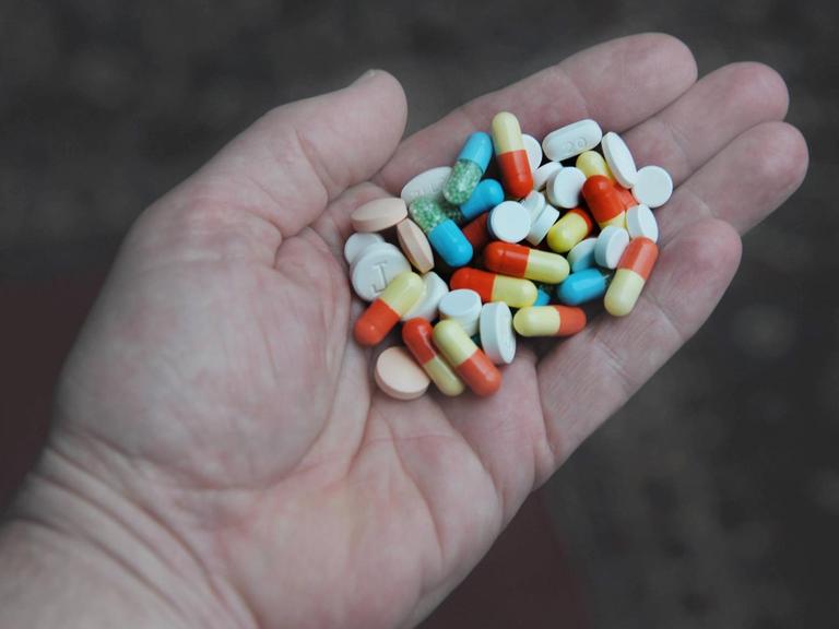In einer Hand liegen viele verschiedenfarbige Tabletten.