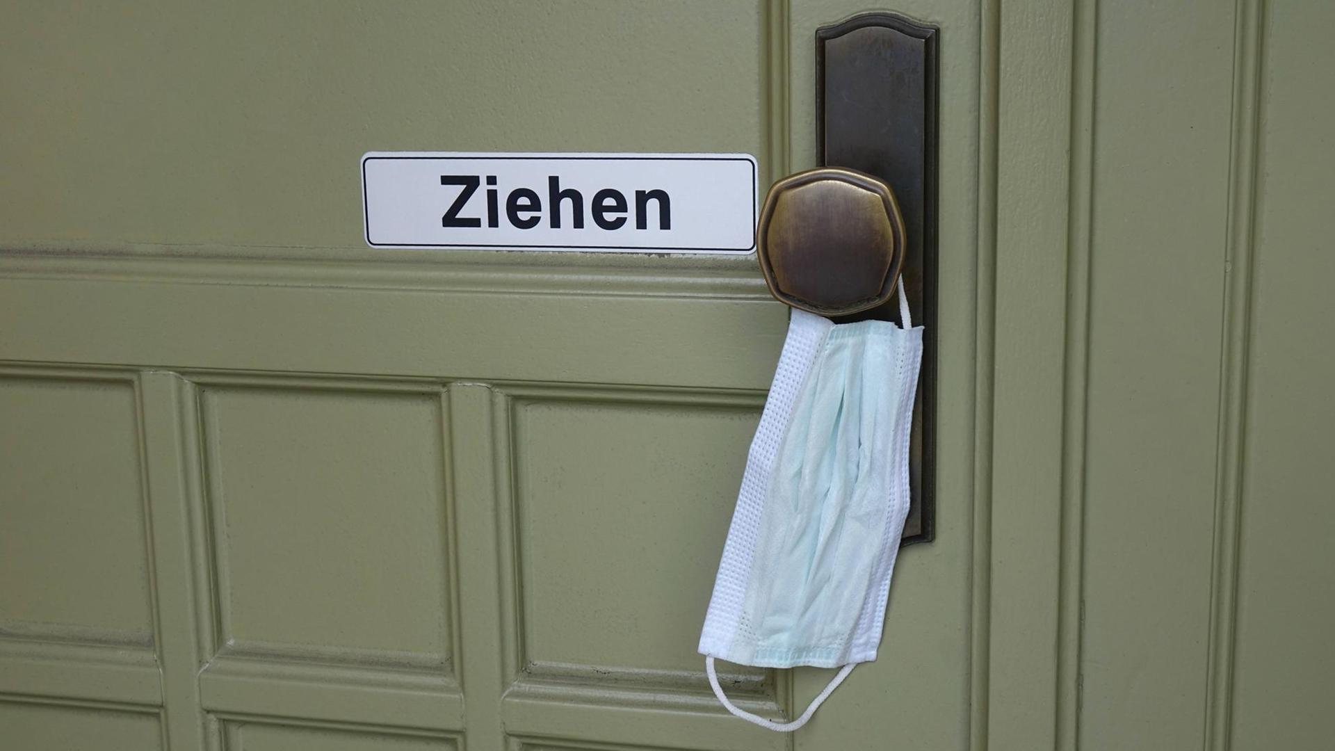 An einer Türklinke hängt zum Öffnen eine Atemschutzmaske