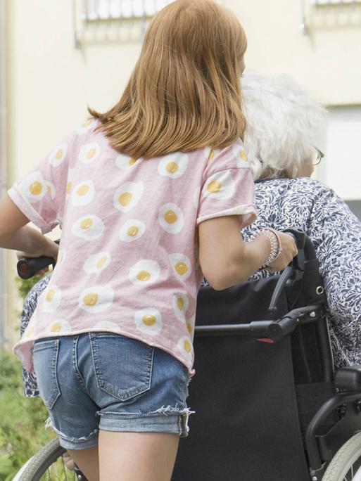 Ein junges Mädchen schiebt den Rollstuhl einer erwachsenen Frau.