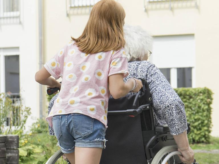 Ein junges Mädchen schiebt den Rollstuhl einer erwachsenen Frau.